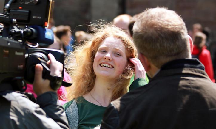 Das Bild zeigt ein blondes Mächen, das vor einer Fernsehkamera von einem Mann interviewt wird.