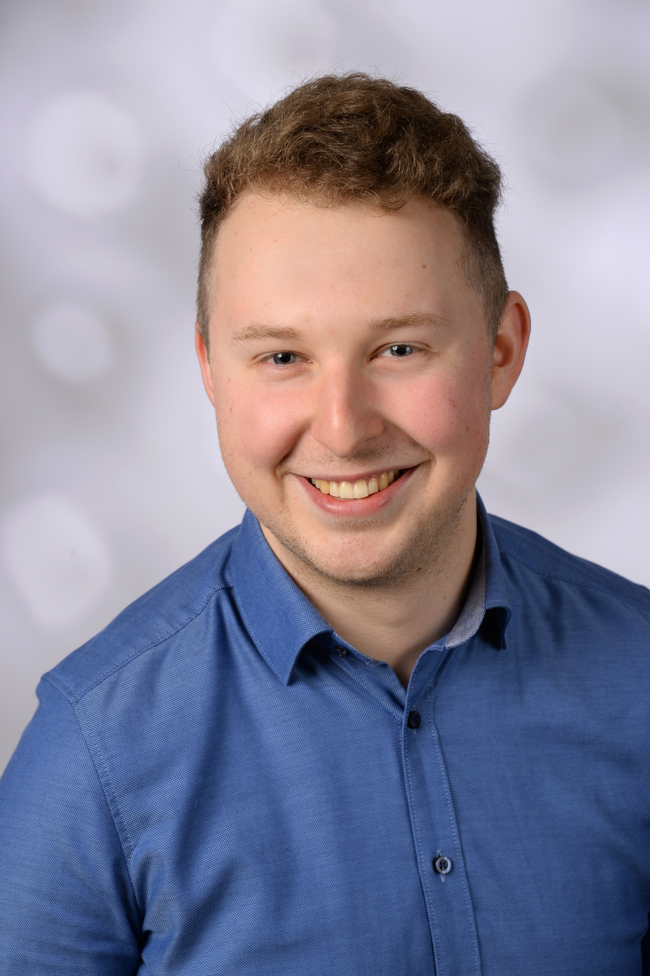 Das Bild zeigt den Organisten Alexander Grün aus Mainz in blauem Hemd vor hellem Hintergrund.