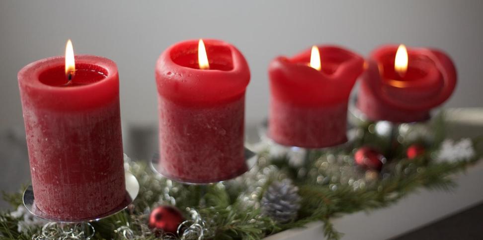 Das Bild zeigt vier rote Adventskerzen auf einer linienförmigen Unterlage aus Tannenzweigen