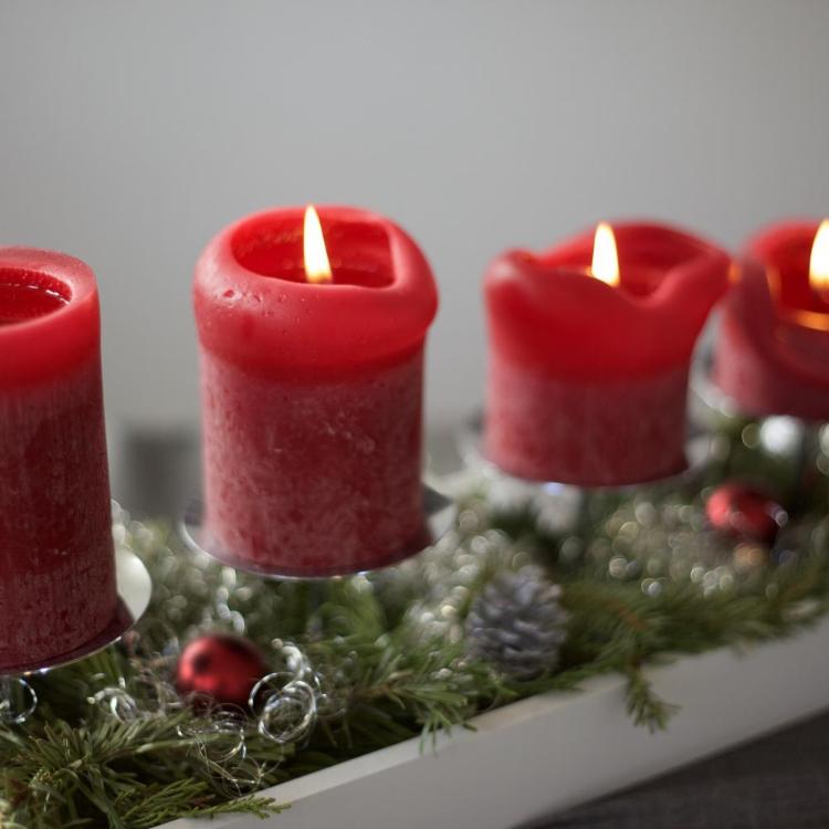 Das Bild zeigt vier rote Adventskerzen auf einer linienförmigen Unterlage aus Tannenzweigen