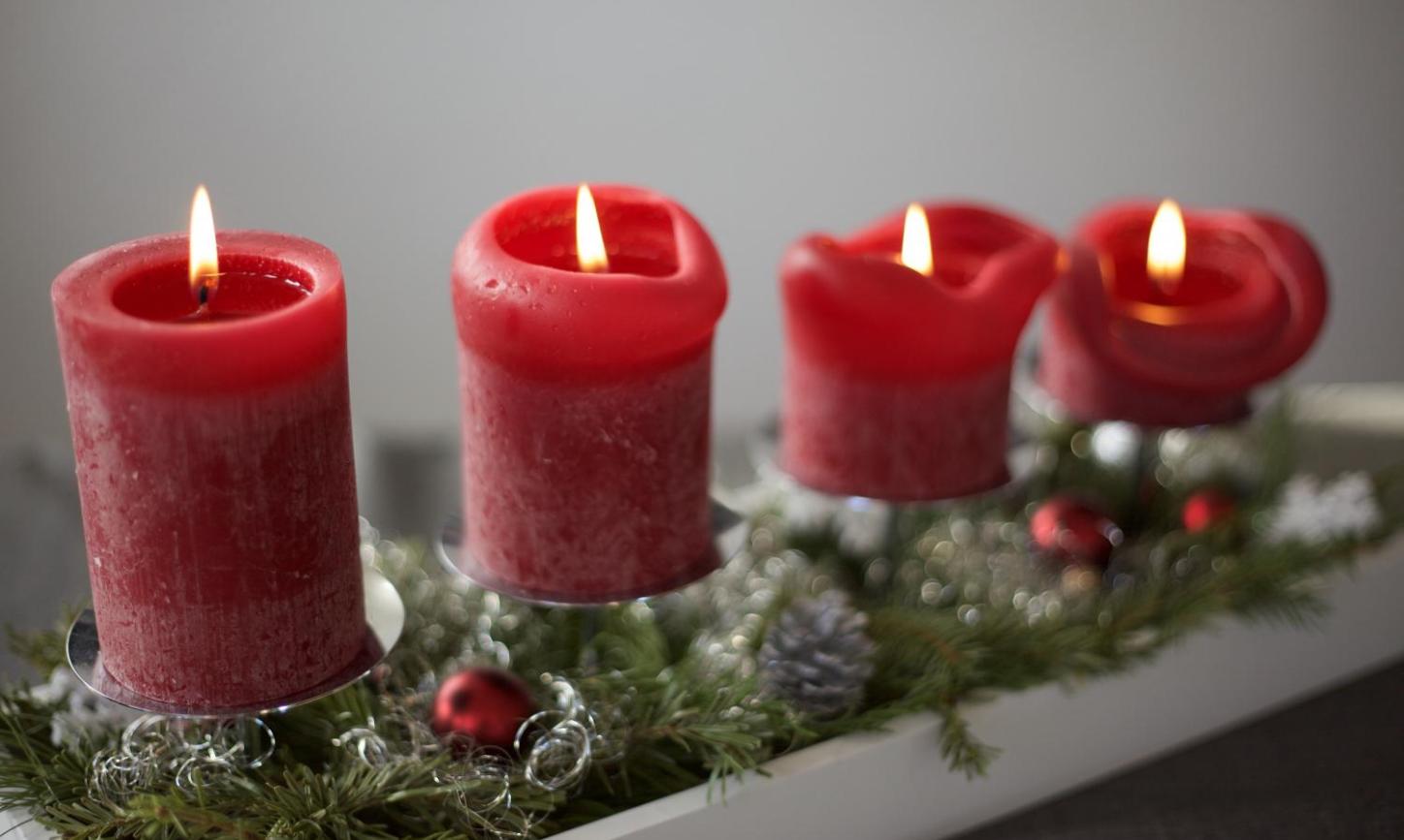 Das Bild zeigt vier rote Adventskerzen auf einer linienförmigen Unterlage aus Tannenzweigen