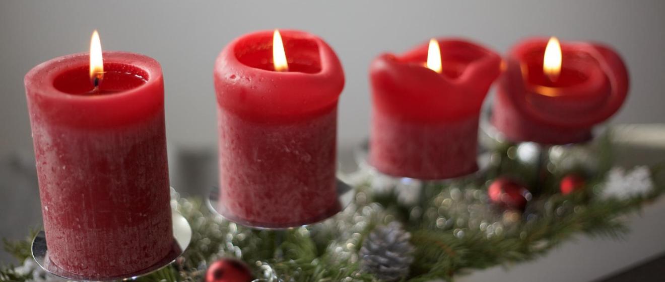 Das Bild zeigt vier rote Adventskerzen auf einer linienförmigen Unterlage aus Tannenzweigen