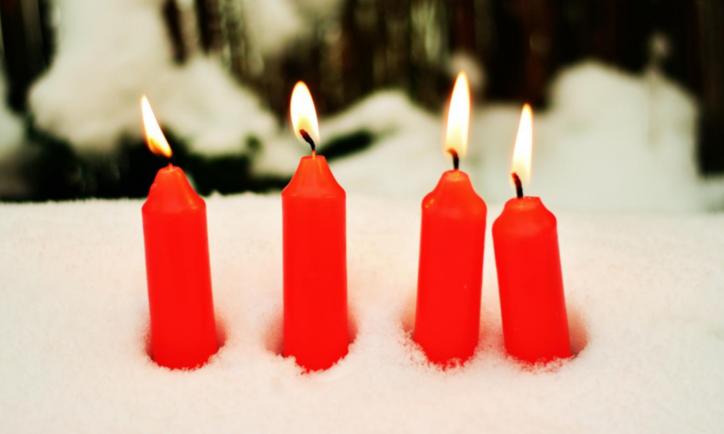 Das Bild zeigt vier rote brennende Kerzen, die im Schnee stecken.