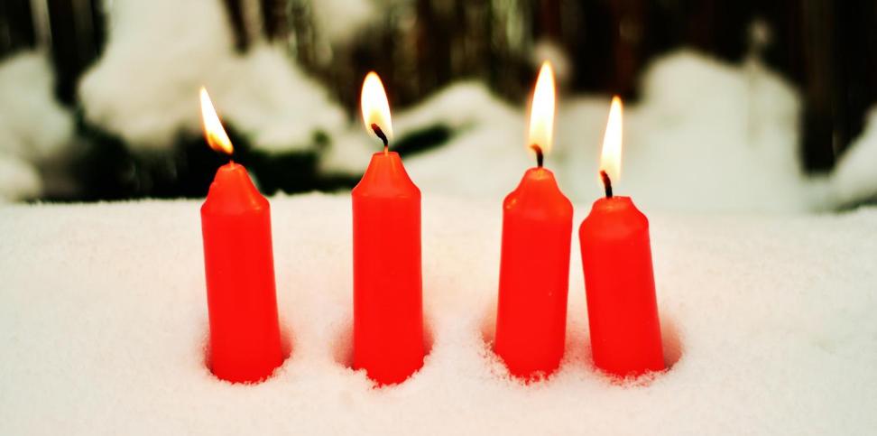 Das Bild zeigt vier rote brennende Kerzen, die im Schnee stecken.