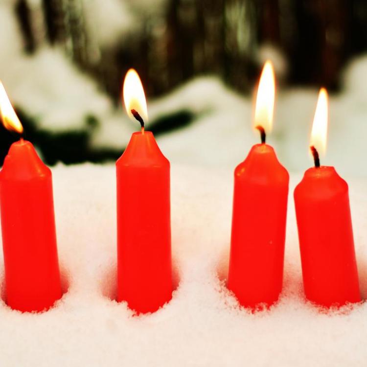 Das Bild zeigt vier rote brennende Kerzen, die im Schnee stecken.