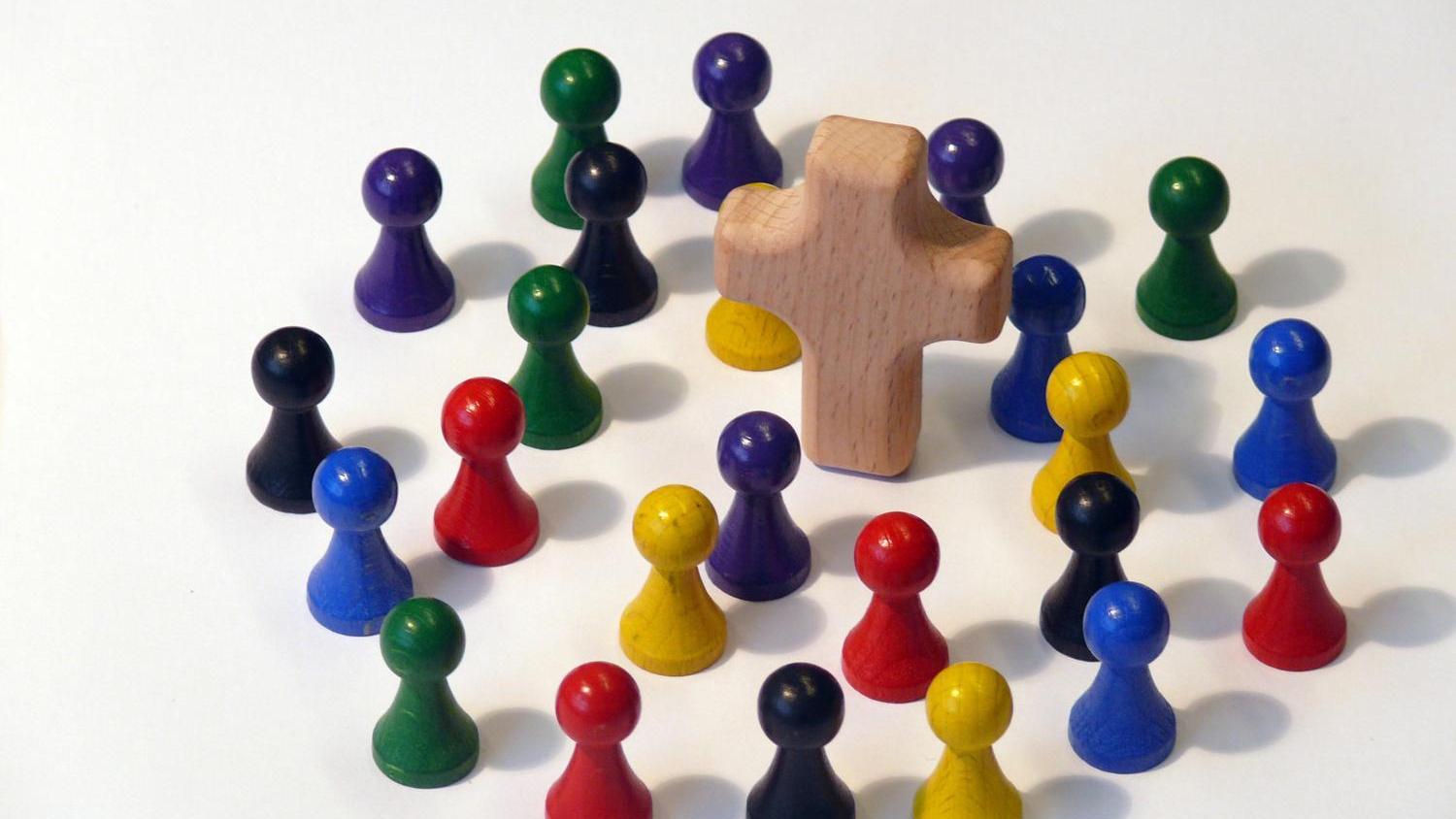 Das Bild zeigt viele bunte Spielfiguren, die im Kreis um Kreuz gruppiert sind.