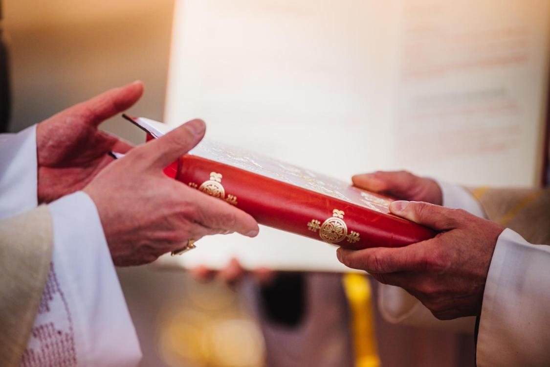 Das Bild zeigt die Hände des Bischofs, der dem angehenden Diakon das Evangelienbuch überreicht.