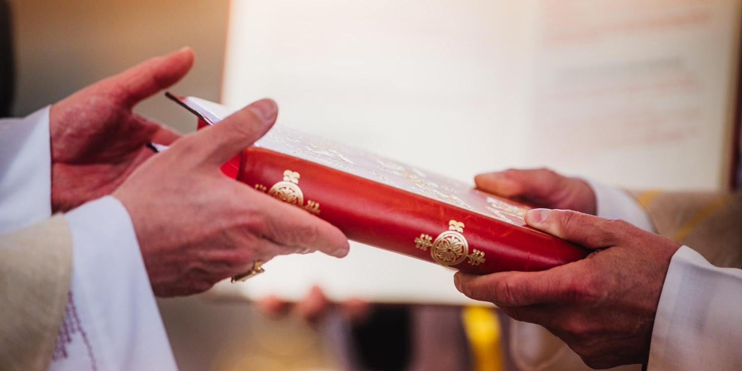 Das Bild zeigt die Hände des Bischofs, der dem angehenden Diakon das Evangelienbuch überreicht.