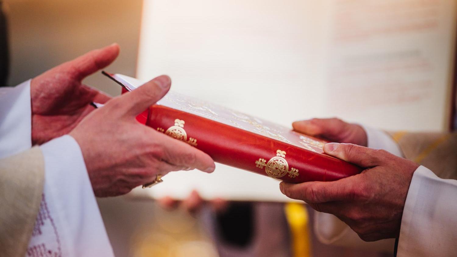 Das Bild zeigt die Hände des Bischofs, der dem angehenden Diakon das Evangelienbuch überreicht.
