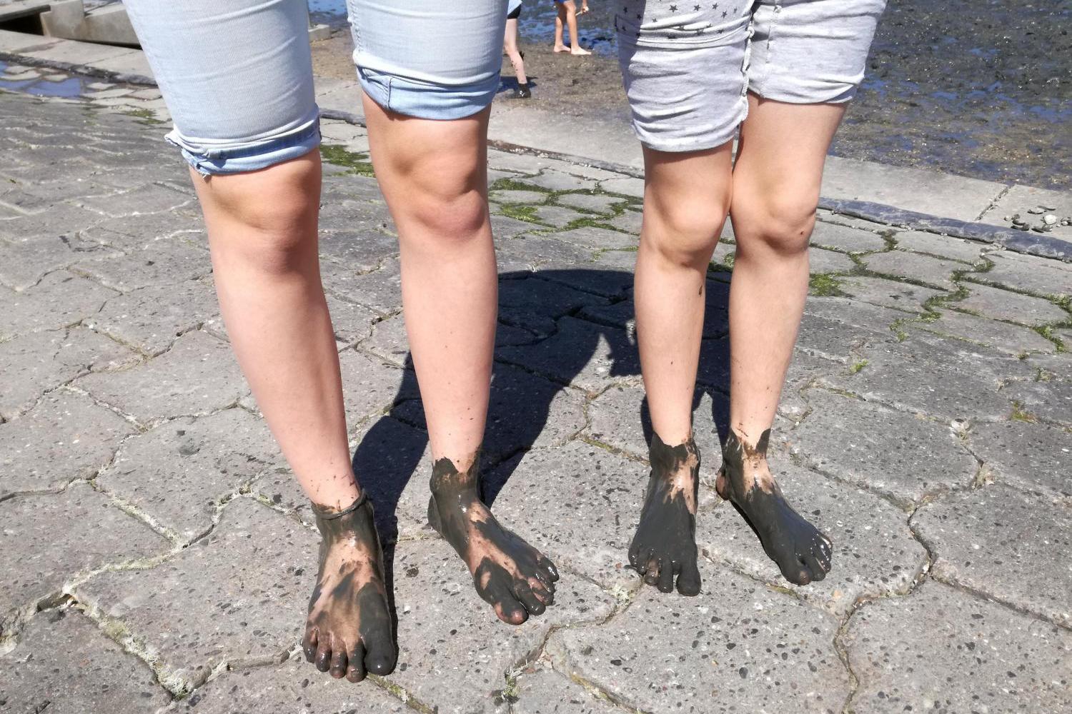 Zwei Personen mit schlammigen Füßen stehen barfuß auf Pflastersteinen.