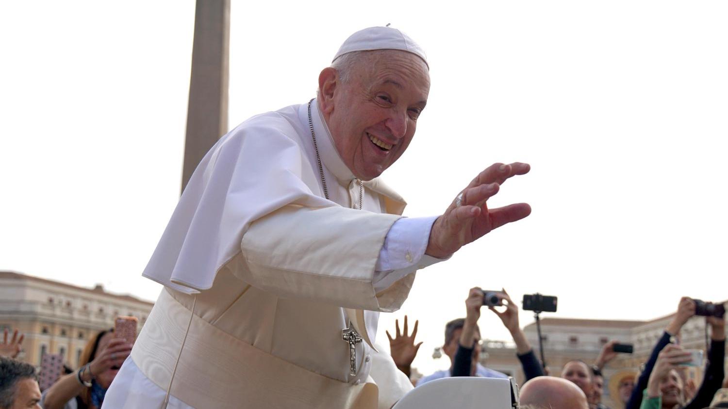 Das Bild zeigt, wie Papst Franziskus bei einer Fahrt durch die Menschenmenge grüßt