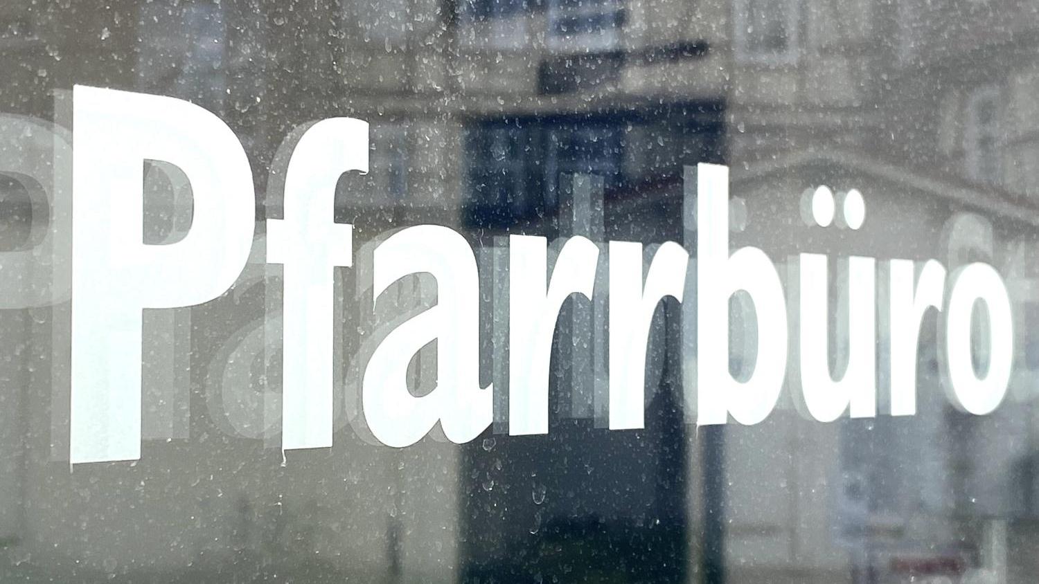 Das Bild zegt den Ausschnitt einer Glastür mit dem Schriftzug 'Pfarrbüro'
