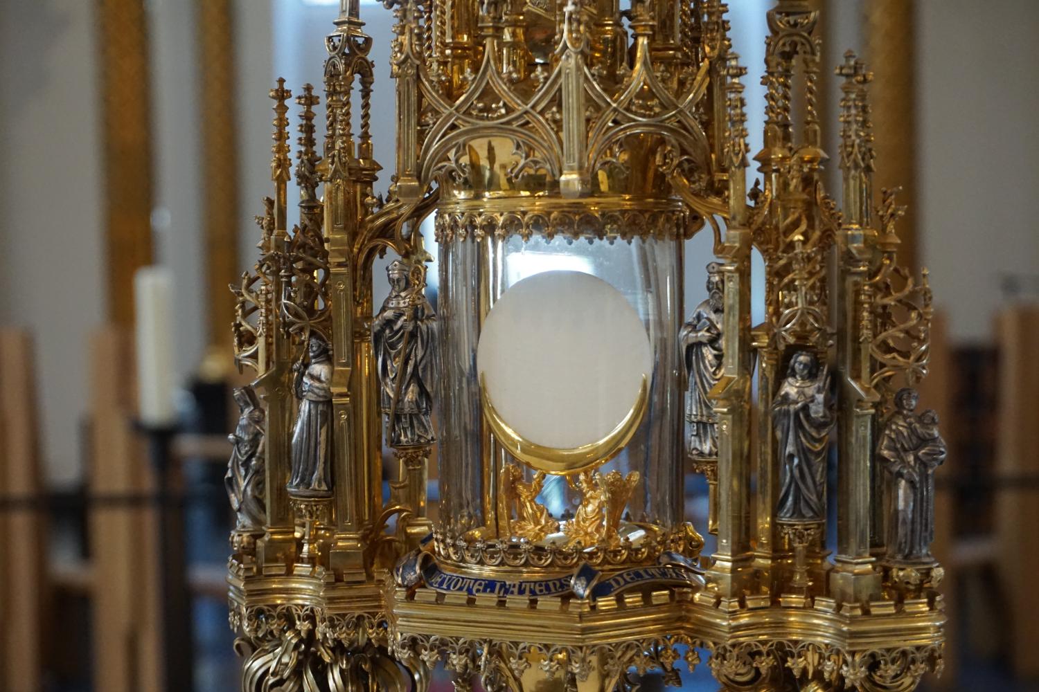 Vergoldete Monstranz mit Hostie, umgeben von Heiligenfiguren in einer Kirche.