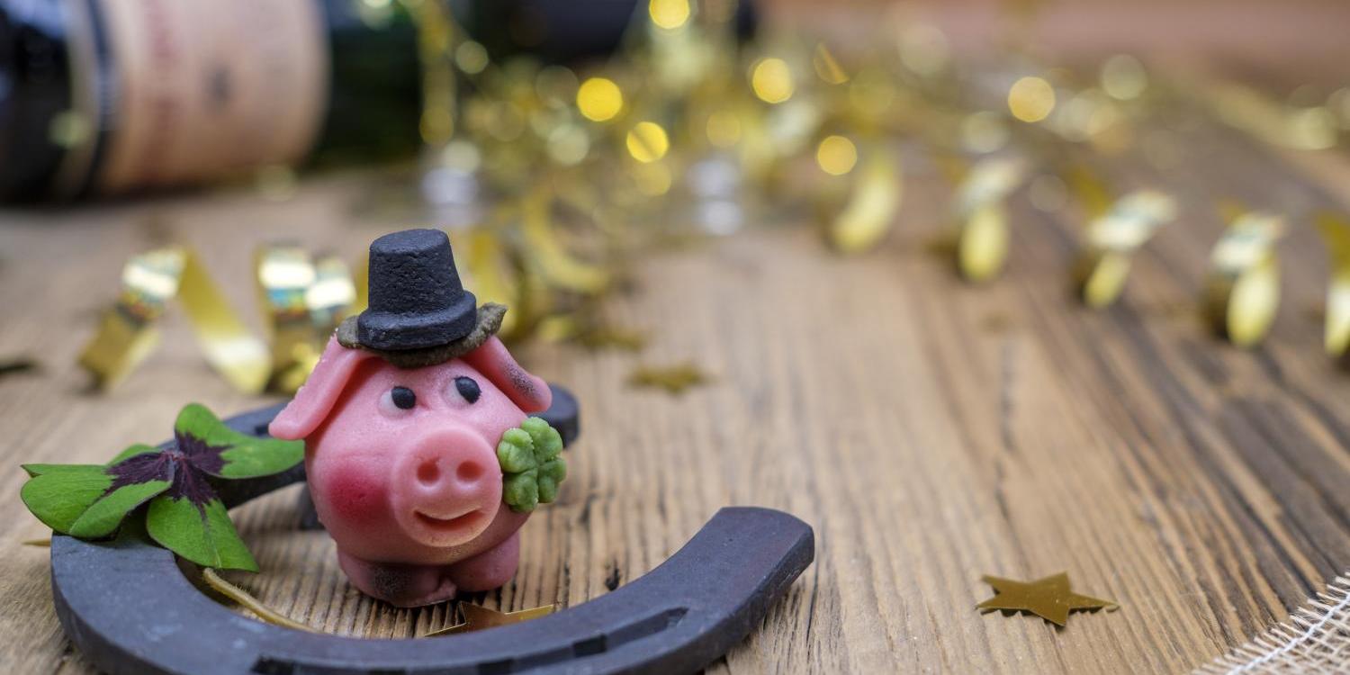 Das Bild zeigt ein Hufeisen mit Glücksklee und Glücksschwein auf einem Tisch liegend vor einer Weinflasche