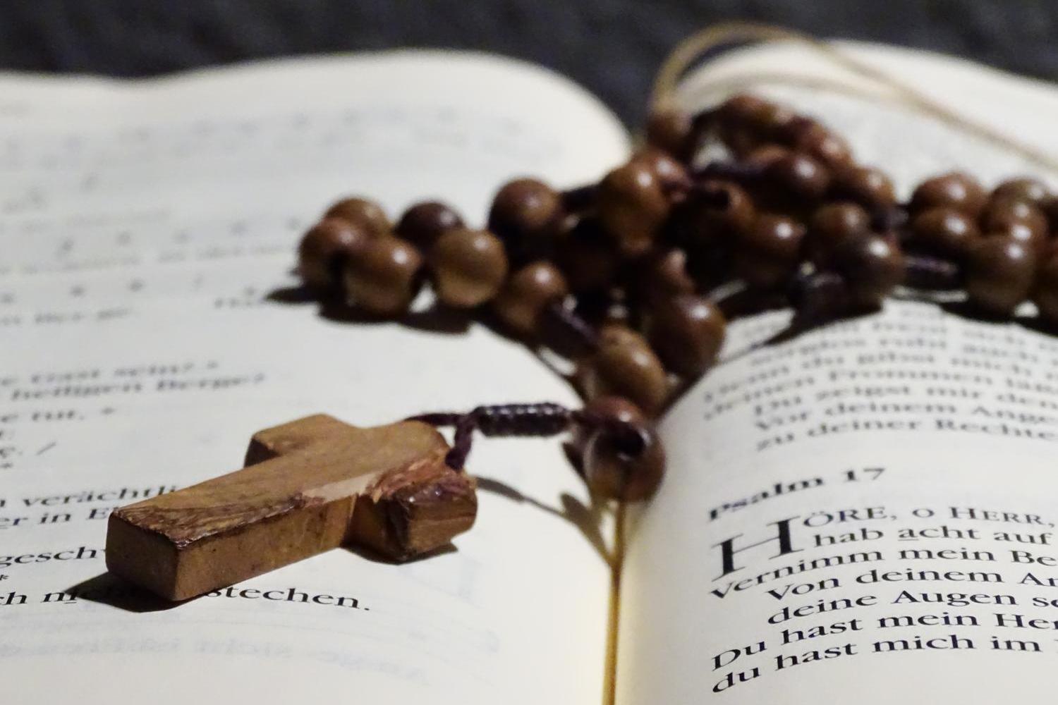 Holzrosenkranz mit Kreuz liegt auf aufgeschlagenem Buch.